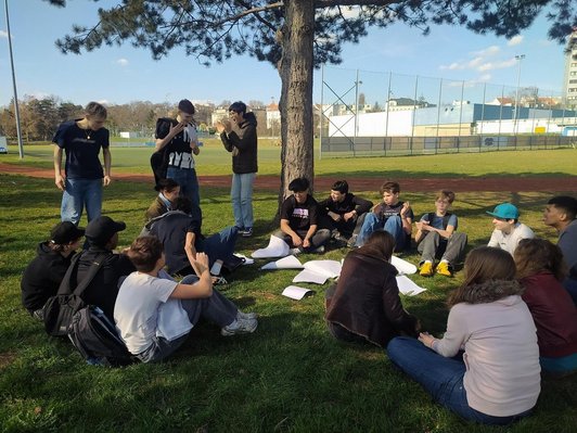Foto von mehreren Schüler:innen auf einer Wiese bei einem Sportplatz