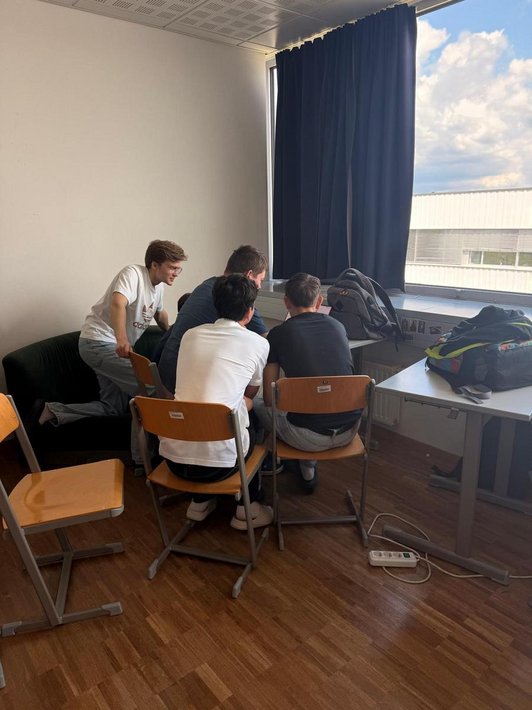 Vier Schüler sitzen an Tisch und blicken auf Laptop-Bildschrim