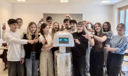 Foto von Jugendlichen einer Klasse mit einem selbst gebastelten Alu-Roboter in der Mitte.