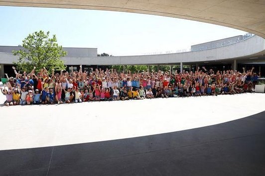 Schüler/innen sitzen und stehen mit nach oben gesteckten Händen in Gruppe vor dem Schuleingang