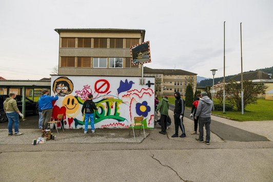 Jugendliche mit Hanschuhen und Masken, einige besprühen eine Wand mit Graffiti