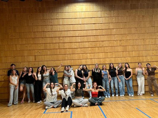 Mädchen einer Klasse stehen vor einer Holzwand im Turmsaal und heben die Arme "Zusammen sind wir stark".