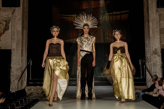 Foto der Fashionshow. 3 Schülerinnen in gold/schwarz gekleidet.