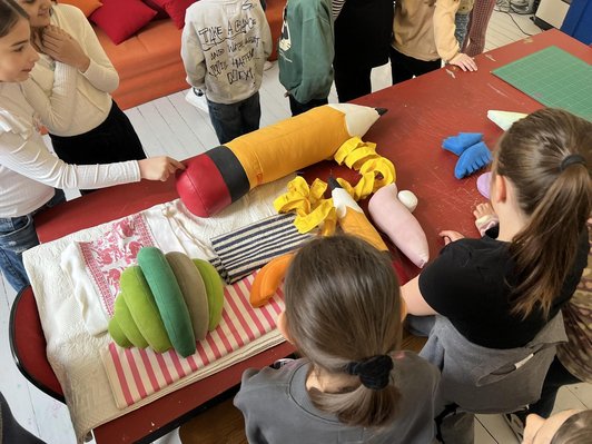 Tisch mit Stoff-Striften und Textilien umgeben von Schüler/innen