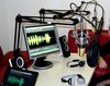 Foto einer technischen Station einer Radioproduktion mit drei Mikrofonen, je zwei Kopfhörern, Lautsprechern und Screens 