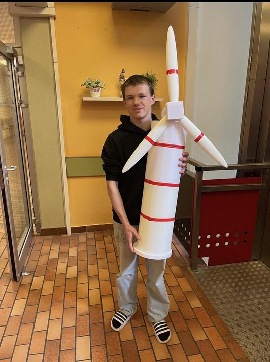 Foto von einem Schüler mit einem selbst gebauten Windrad weiss mit roten Streifen in der Hand.