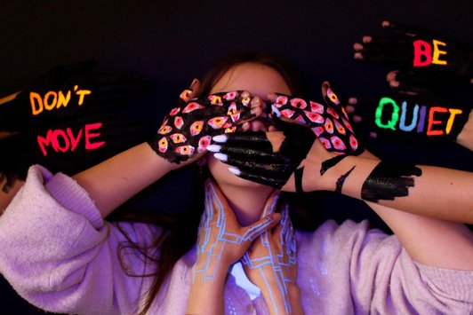 Foto einer Schülerinn mti bunt neonfarben mit bemalten Händen mit Augen vor dem Gesicht und am Hals