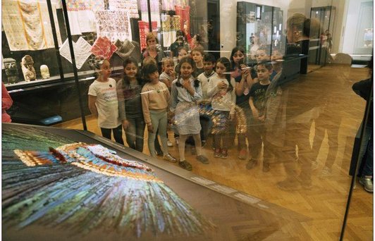 Kinder stehen vor einer Vitrine mit einem historischen Kopfschmuck.