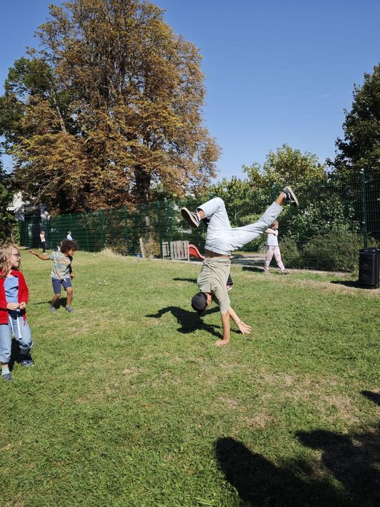 Ein Junge macht auf einer Wiese einen Handstand, zwei Kinder schauen ihm zu.