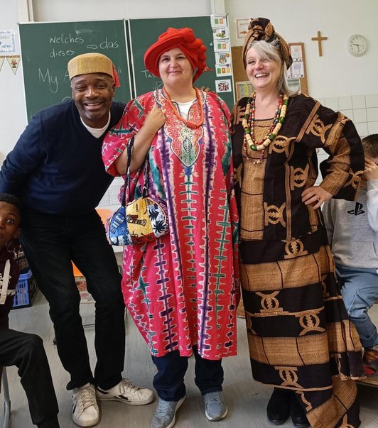 Zwei Frauen und ein Mann in aftikanischer Tracht in Klassenzimmer