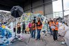 Jugendliche mit orangenen Warnwesten und Filmkamera vor einem riesigen Müllberg