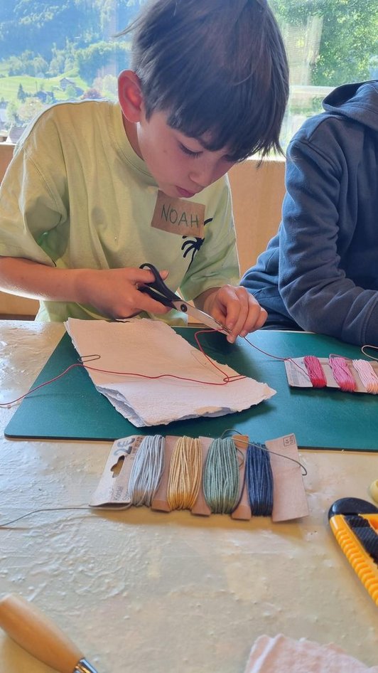 Schüler an Tisch mit Buchbinde-Material schneidet Faden mit Schere