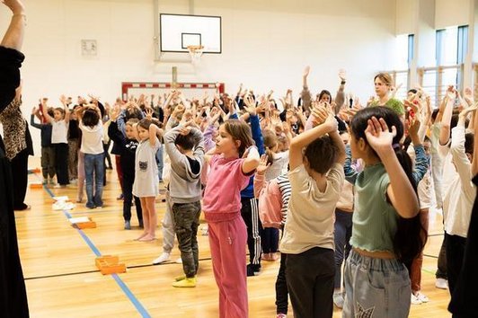 viele Kinder mit erhobenen Händen in Turnsaal