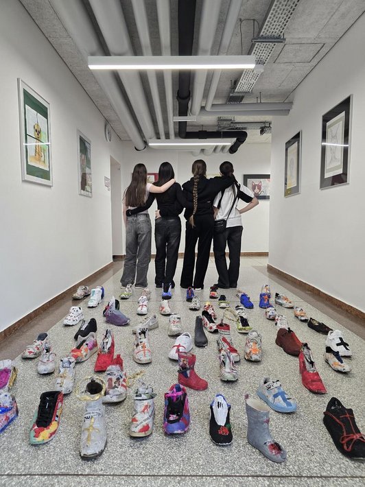 Foto voneinem Schulgang mit 4 Jugendlichen stehend von hinten. Davor auf dem Boden viele bemalte bunte Schuhe.