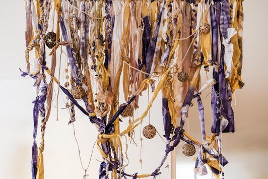 Schnüre, gefärbte Bänder hängen von der Wand und sind ineinander verstrickt.