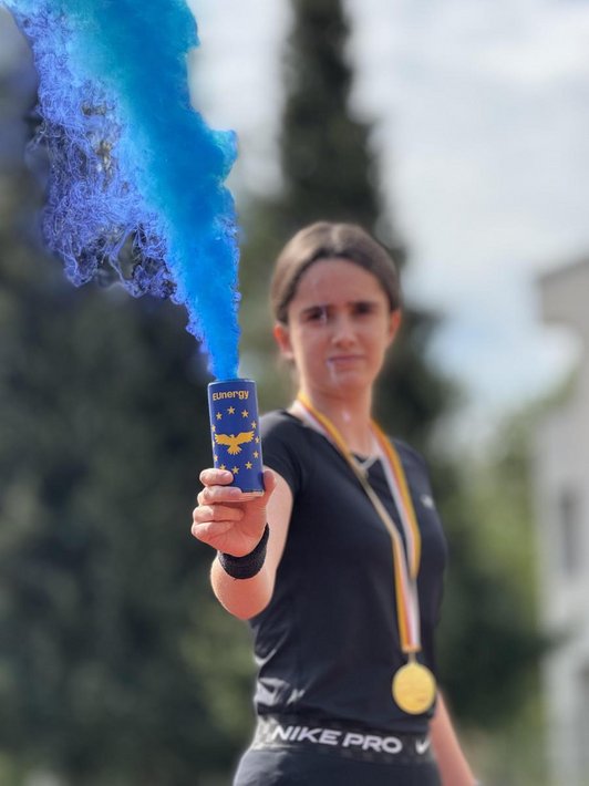 Foto einer Schülerin die einen Energydrink mit dem Zeichen der Europäischen Union hält, aus dem blauer Rauch aufsteigt