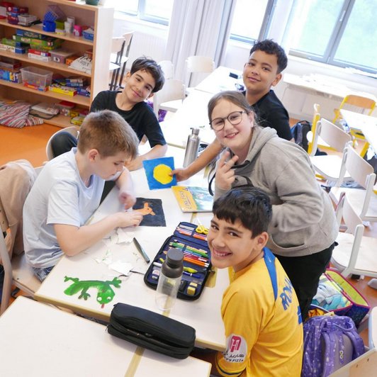 fünf Schüler/innen um einen Tisch mit Stiften und Zeichnungen