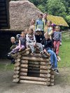 14 Schüler/innen sitzen und stehen auf einem kleinen Blockhaus.
