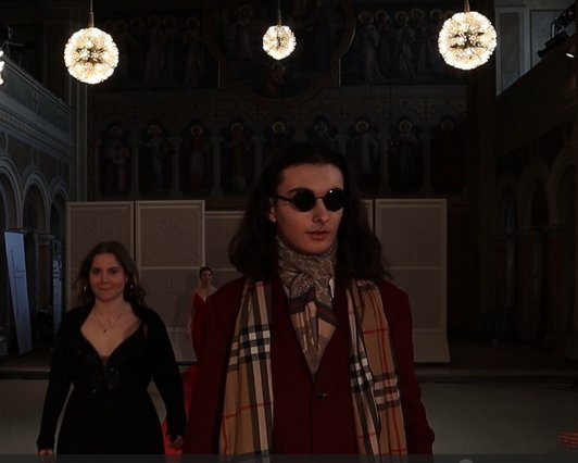Foto einer Szene eine Theaterstückes Schüler mit Sonnenbrille und karriertem Schal. 