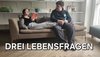 Foto von einer Schülerin liegend auf einer Couch mit Buch, daneben sitzend ein Schüler.