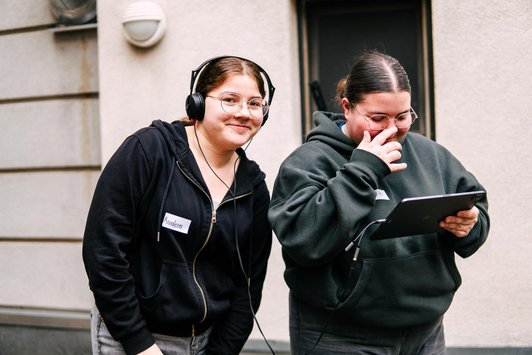 Zwei Schülerinnen, eine hält ein Tablet, die andere trägt die angesteckten Kopfhörer