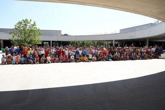 Alle Schüler/innen sitzen und stehen in einer Gruppe zusammen vor dem Schuleingang.