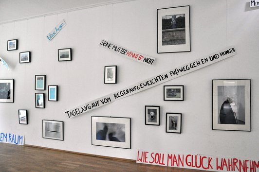 Foto einer Wand der Ausstellung mit gerahmten Fotografien und Spruchbändern